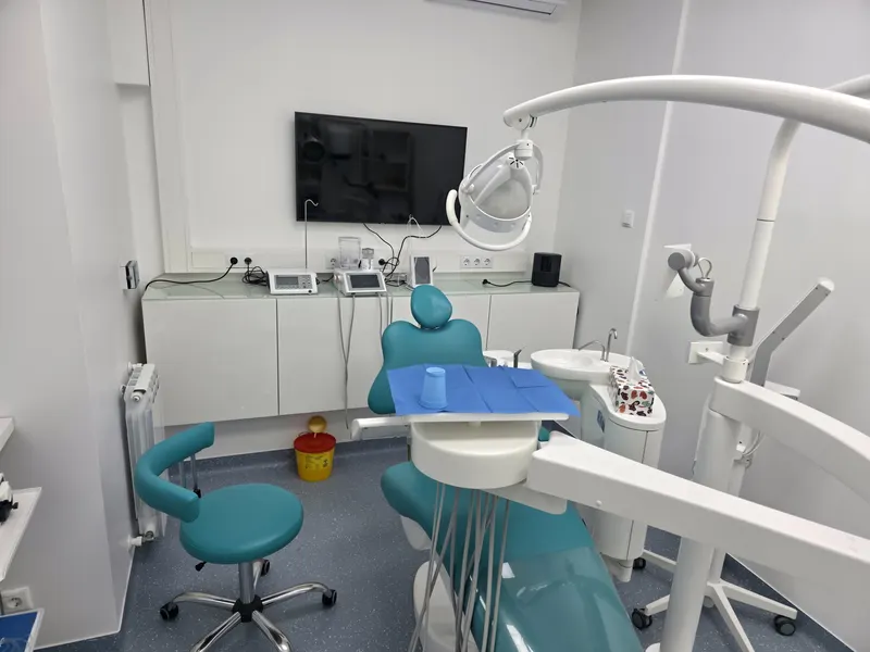 Cabinet cu pereți albi: unit dentar turcoaz, scaun pentru medic și un televizor pe perete