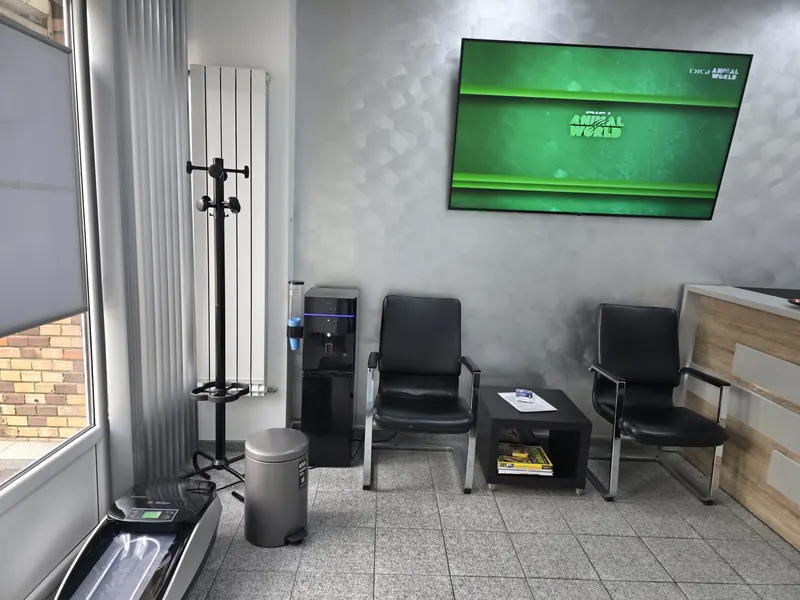 Sala de așteptare: scaune negre, o măsuță, un cuier și un televizor pe perete