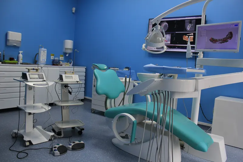 Unit dentar turcoaz cu lampa deasupra, două aparate pe cărucioare și monitoare cu o radiografie și o scanare 3D