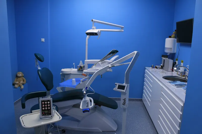 Cabinet cu unit dentar albastru, dulapuri albe și un ursuleț de pluș pe scaun