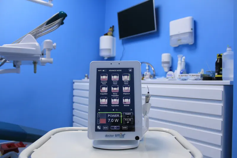 Aparat laser dentar pe un cărucior în cabinet, cu ecranul de setări pentru proceduri pe gingie