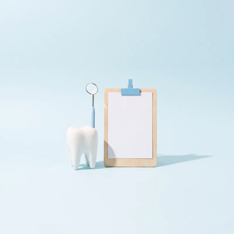 Model de dinte, oglindă dentară și un card alb pe clipboard